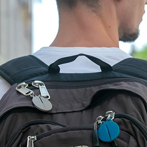 Person wearing a backpack with two round keychain accessories attached.