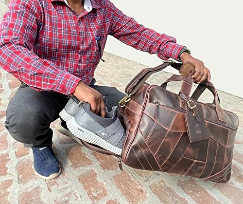 Man packing gray shoes into a brown leather travel bag.