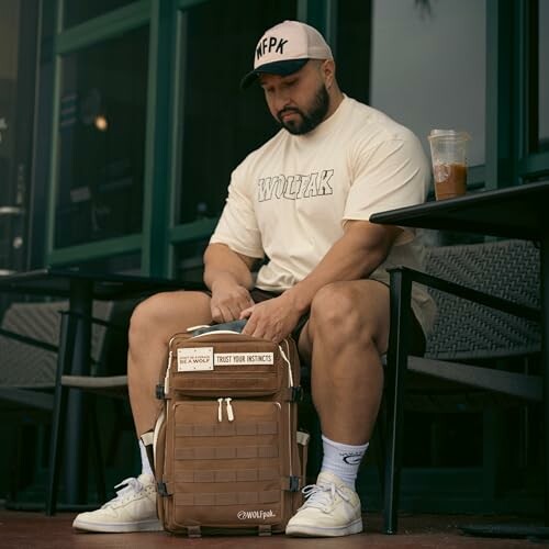 Man sitting at a cafe with a backpack and drink.