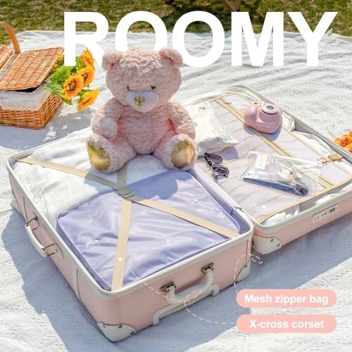 Open suitcase with teddy bear and picnic items on a blanket.